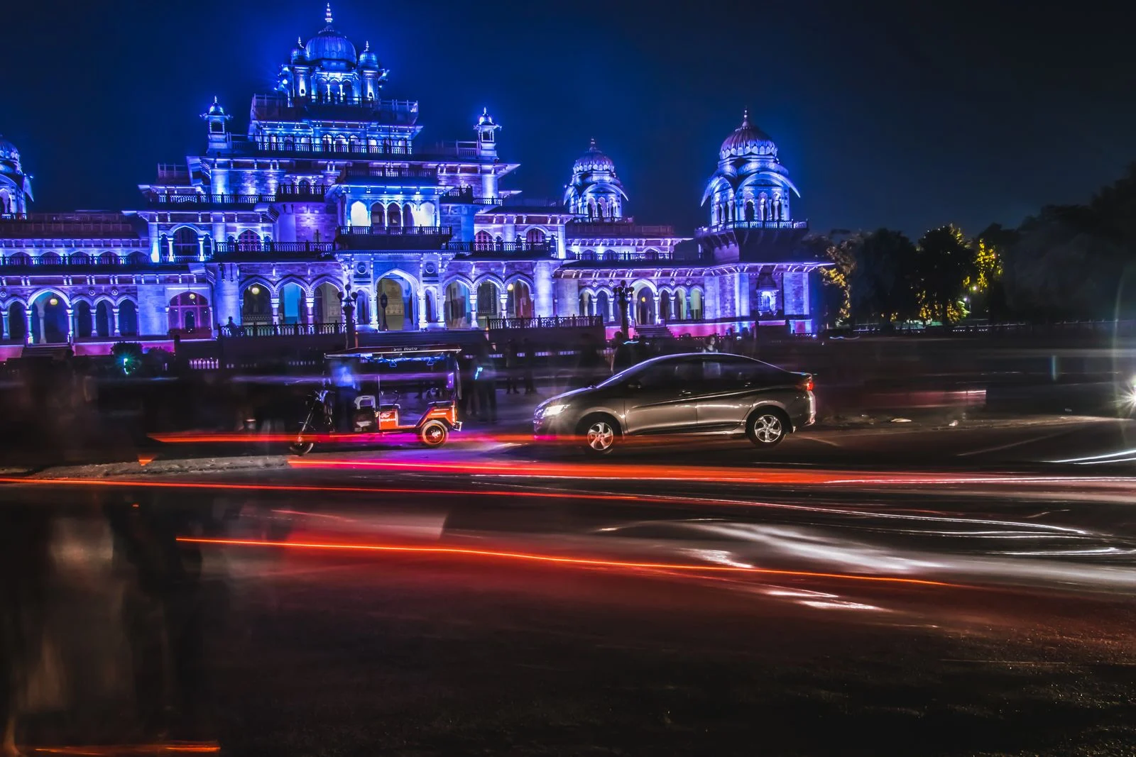 Sedan and auto rickshaw passing the illuminated Albert Hall Museum in Jaipur